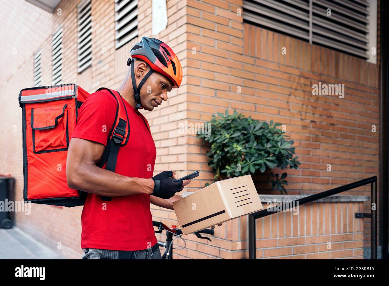 Afrikanischer Bote Mann, der das Paket für die Lieferung am Ziel vorbereitet und sein Telefon benutzt. Stockfoto