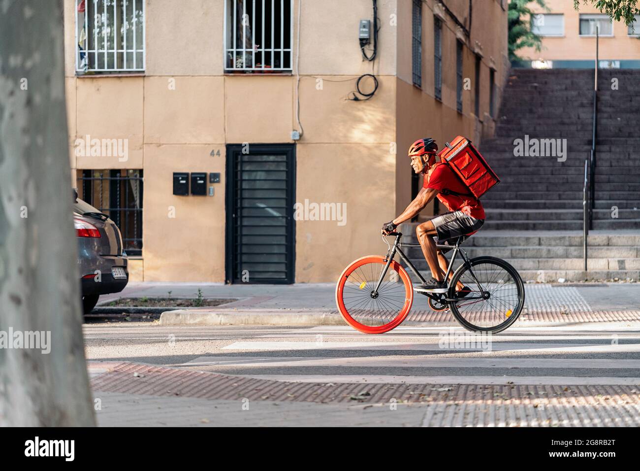 Afrikanischer Lieferer mit Schutzhelm, der in der Stadt auf seinem Fahrrad unterwegs war, um ein Paket zu liefern. Stockfoto