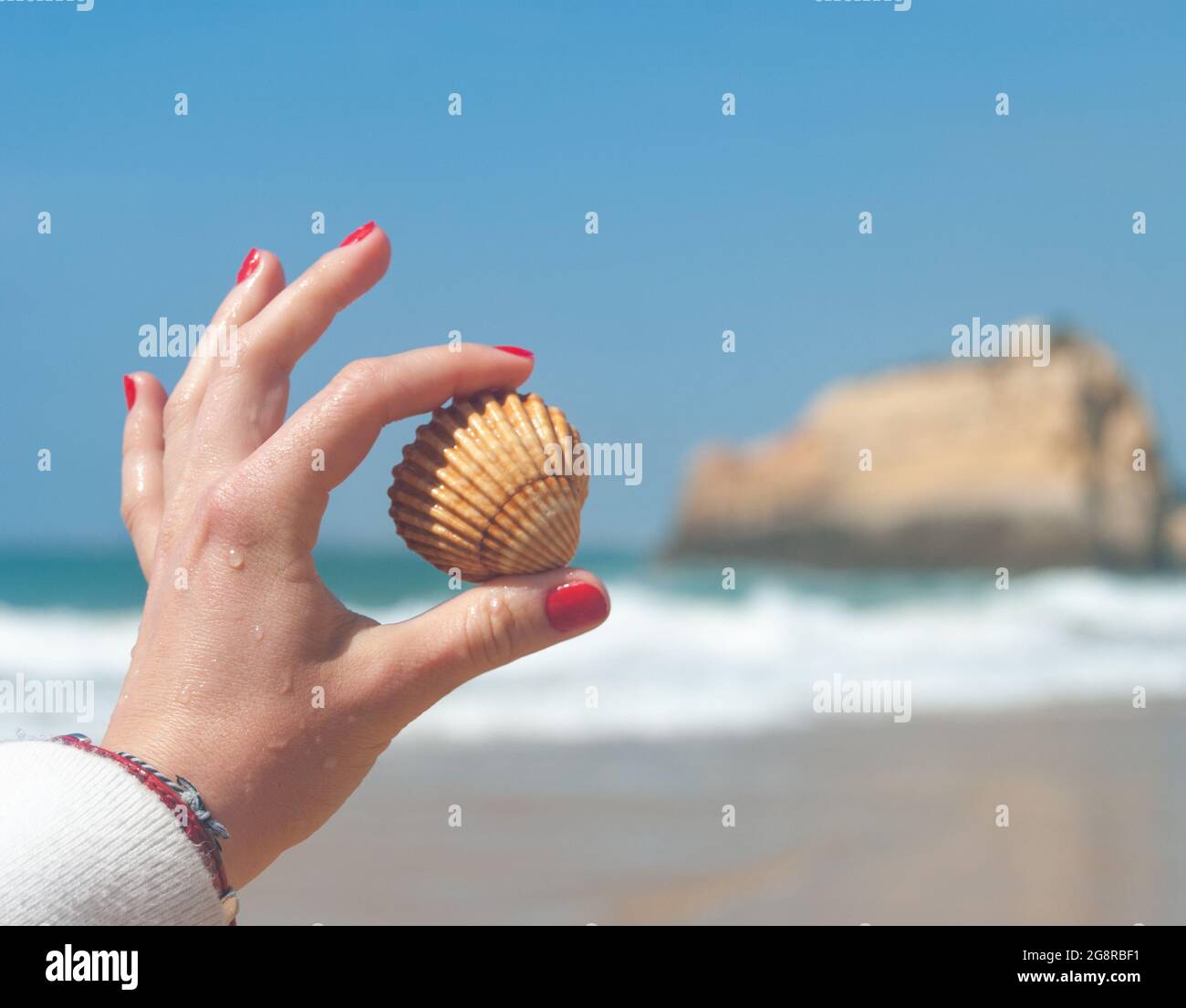 Eine Schale zwischen den Fingern der Frau, rote Nägel und eine wunderschöne Aussicht auf das Meer im Hintergrund - Platz für Text, selektiver Fokus Stockfoto