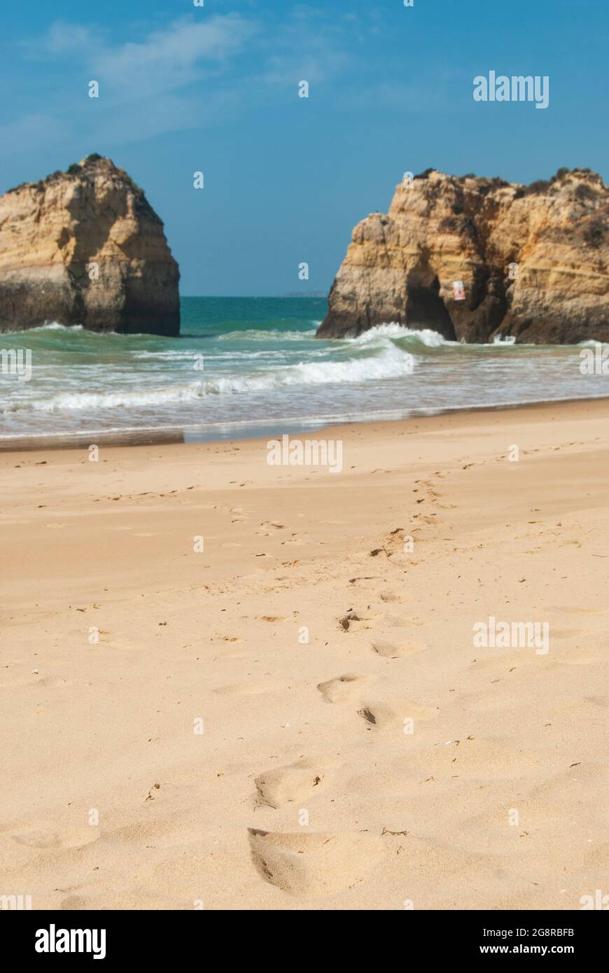 Nahaufnahme der Fußabdrücke im Sand eines leeren Strandes, Klippen im Ozean im Hintergrund, blauer Himmel - selektiver Fokus, Platz für Text Stockfoto