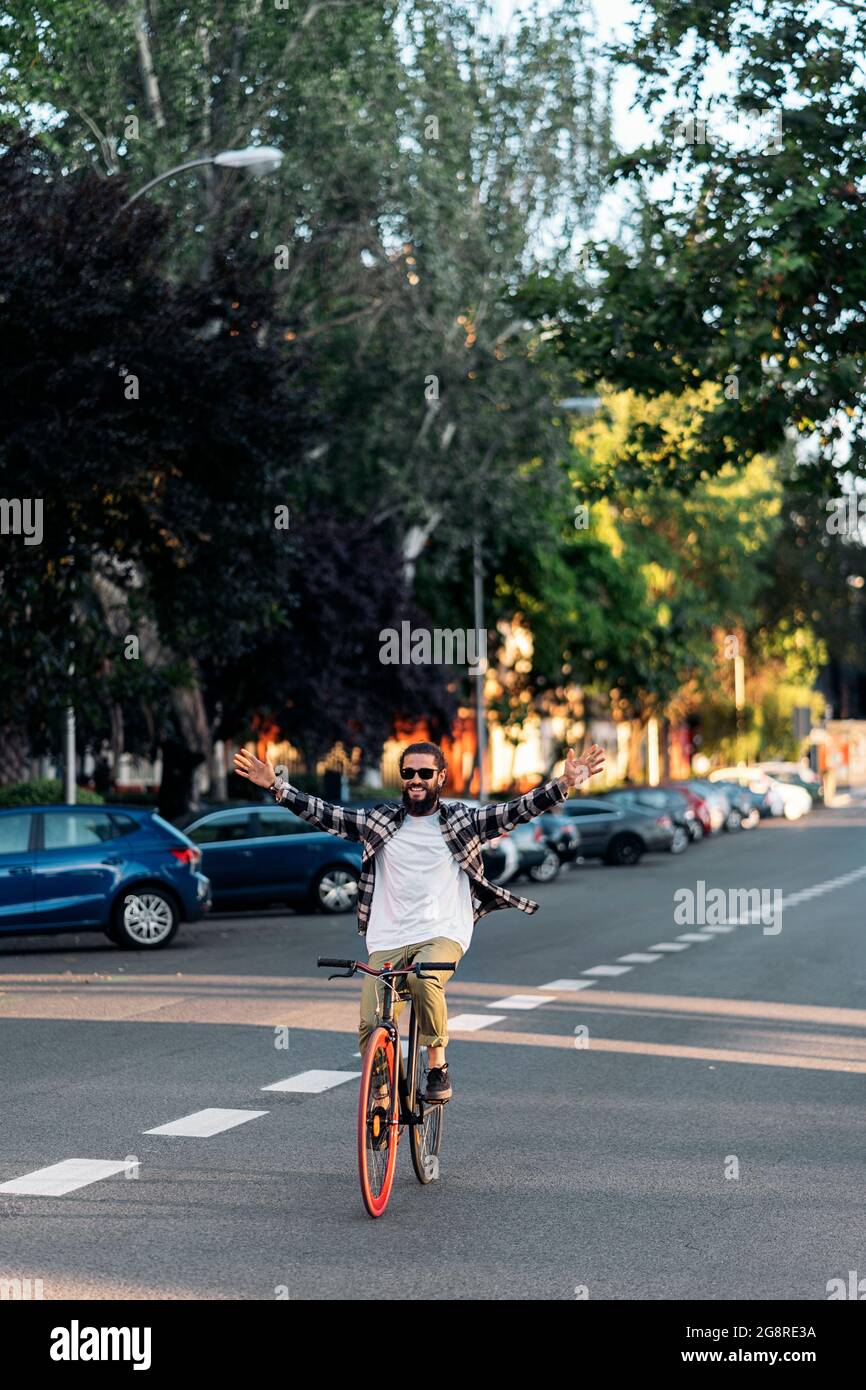 Glücklicher Hipster-Mann mit großem Bart, der in der Stadt Fahrrad fährt und die Arme hebt. Stockfoto