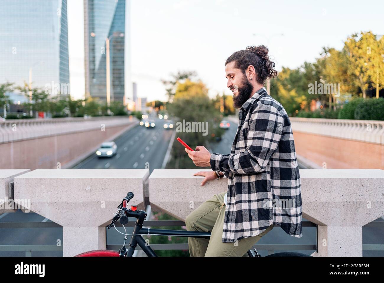Glücklicher Hipster-Mann, der in seinem Fahrrad sitzt und sein Mobiltelefon benutzt. Er ist in der Stadt. Stockfoto