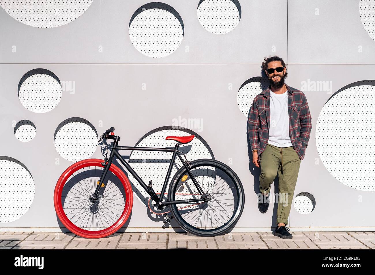 Glücklicher Mann mit langem Bart, der mit seinem coolen Fahrrad auf der Straße steht und die Kamera anschaut. Stockfoto