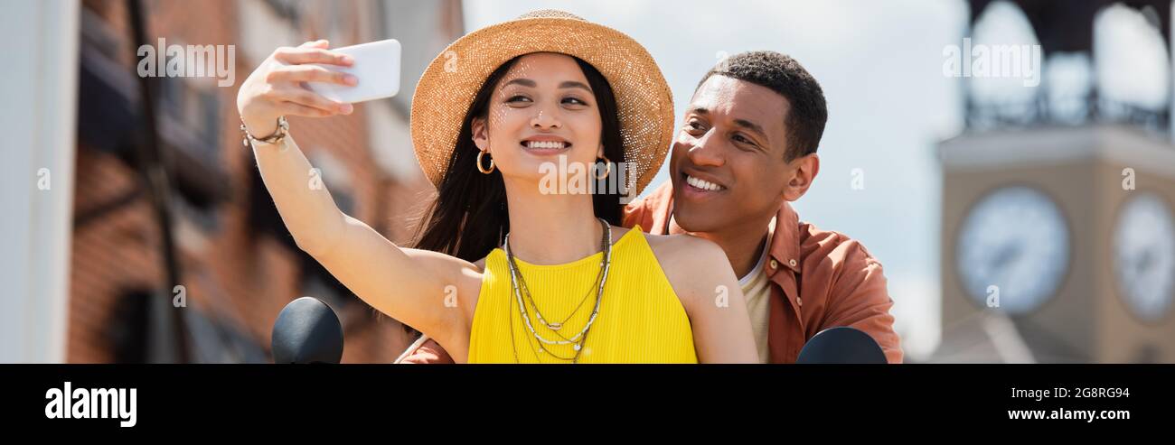 Glückliche asiatische Frau, die Selfie mit afroamerikanischem Mann im Freien macht, Banner Stockfoto