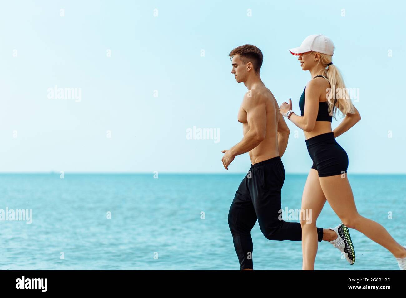 Junges Paar läuft am Strand, Athletic Attraktive Menschen Joggen in Sommer-Sportbekleidung, am Meer, Ausübung ihrer gesunden Lebensweise Stockfoto