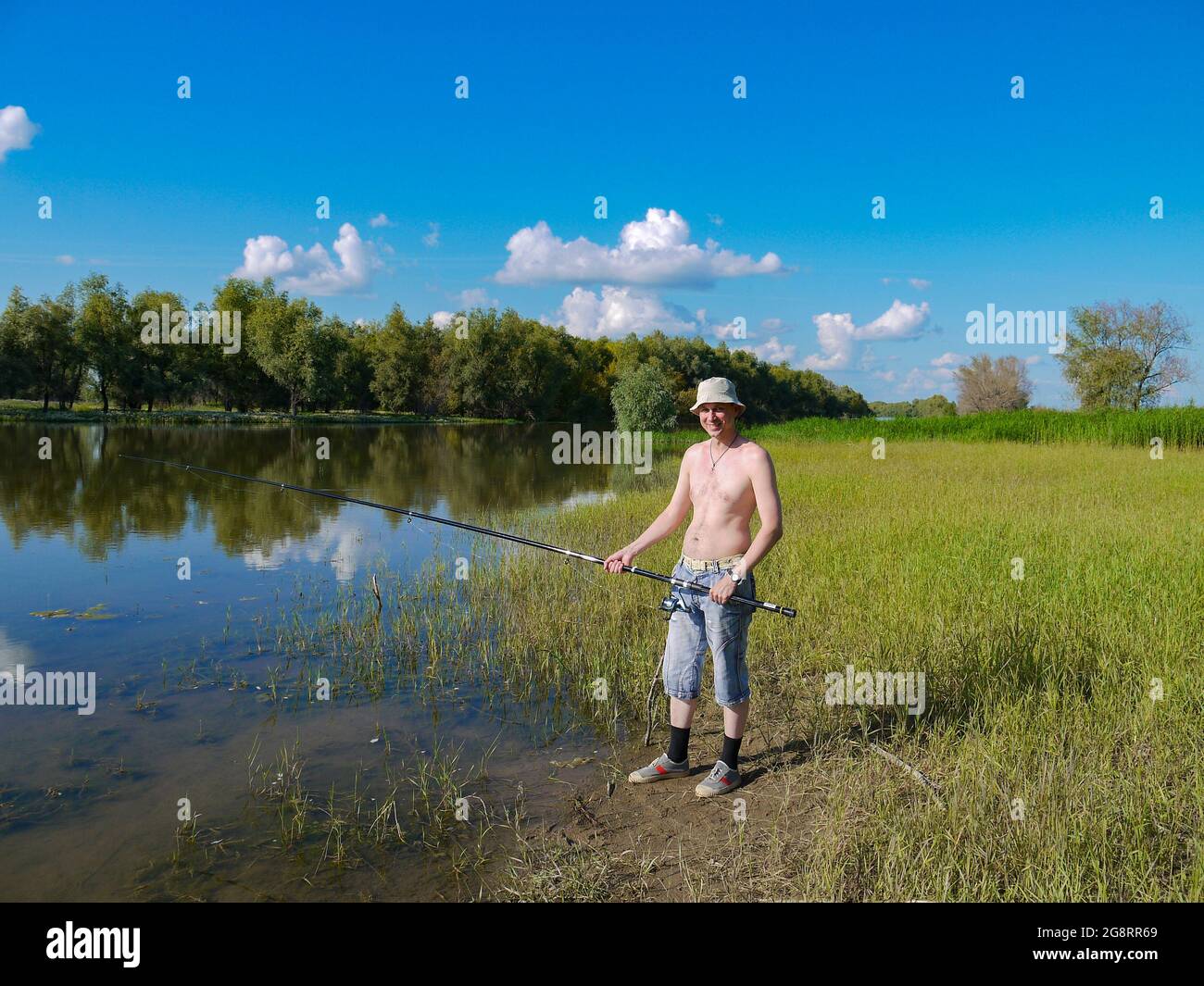 Ein Mann mit einer Angelrute fischt auf einem Fluss im Dorf. Das Konzept eines gesunden Lebensstils in der Natur. Stockfoto