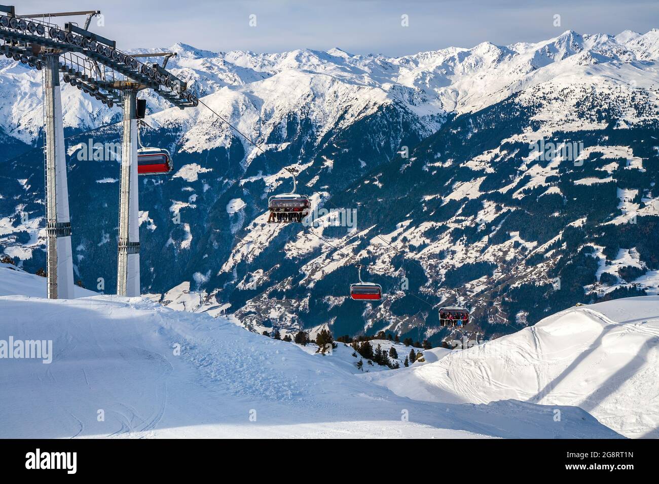 Sessellift in den Alpen vor der Kulisse von Berggipfeln. Skifahrer und Snowboarder erklimmen die Piste mit der Seilbahn. Skigebiet in Österreich, Zillert Stockfoto