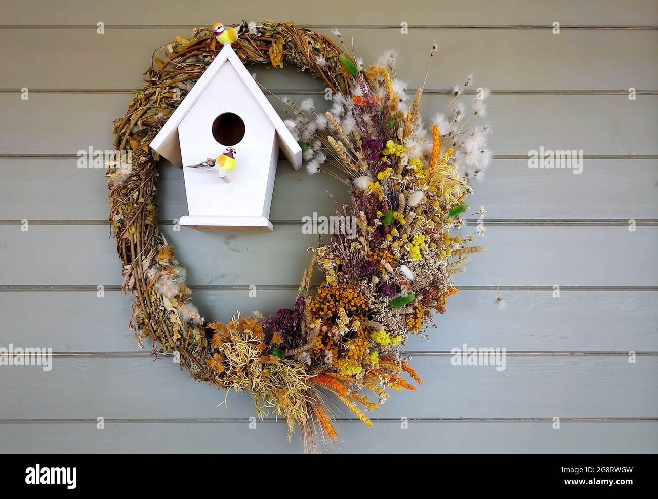 An der Hauswand hängt ein Vogelhaus mit künstlichen Vögeln, die mit einem  Kranz aus getrockneten Kräutern geschmückt sind Stockfotografie - Alamy