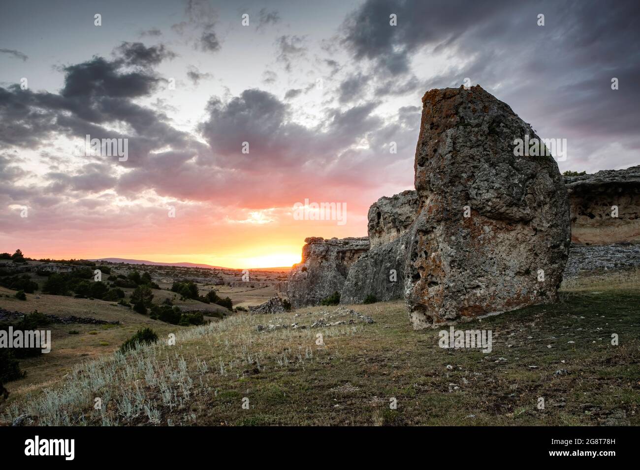 Sonnenuntergang in der Nacht der Sommersonnenwende mit einem megalithischen Menhir im Vordergrund und einer felsigen Gebirgsformation im Hintergrund, Menhir de Camp Stockfoto