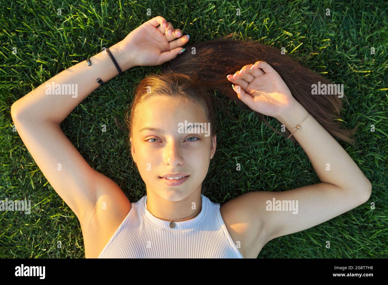 Porträt eines Teenagers, Draufsicht, lächelnd schöne Frau, die auf grünem Gras liegt Stockfoto