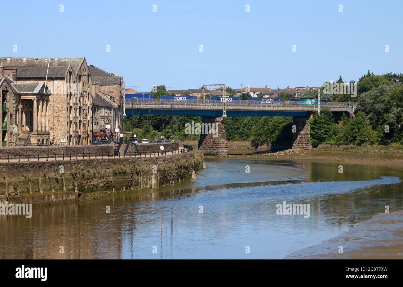 Blick auf den Fluss Lune in Lancaster, vorbei am St. George's Quay, zur Carlisle Bridge mit dem Containerzug auf der West Coast Main Line, 17. Juli 2021. Stockfoto