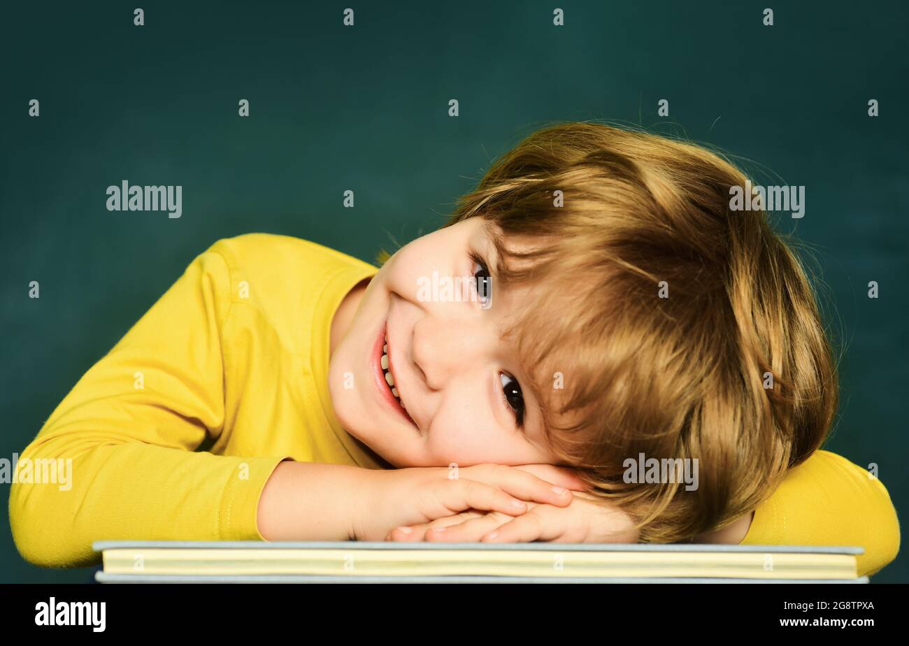 Talentiertes Kind. Netter Junge mit fröhlichem Gesichtsausdruck neben dem Schreibtisch und Schulbedarf. Schulunterricht. Kleine Kinder im Schulunterricht. Stockfoto