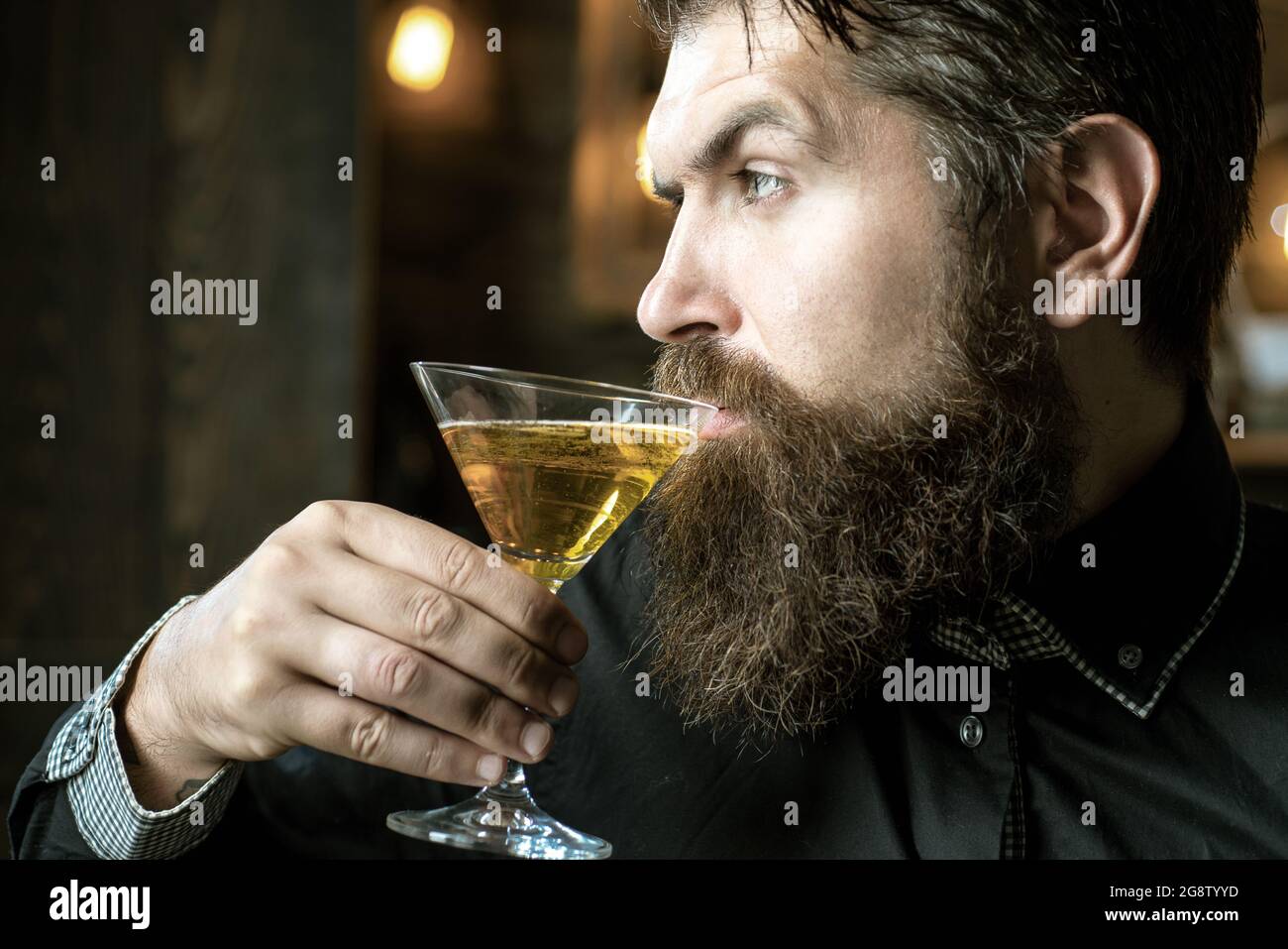 Ein gutaussehender, nachdenklicher Mann hält ein Glas martini in der Hand. Schöner Mann, der Alkohol trinkt, während er an der Bar sitzt. Stockfoto