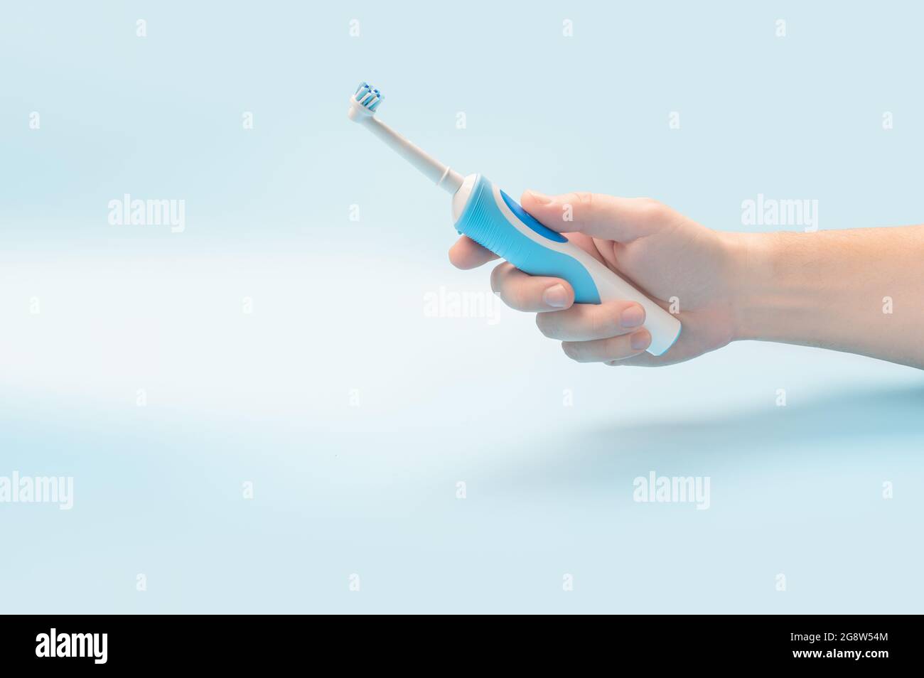 Elektrische Zahnbürste in der Menschenhand. Mann hält elektrische Zahnbürste vor blauem Hintergrund. Moderne Technologie für die Gesundheit. Gesunde Zähne. Zahnmedizin ca. Stockfoto