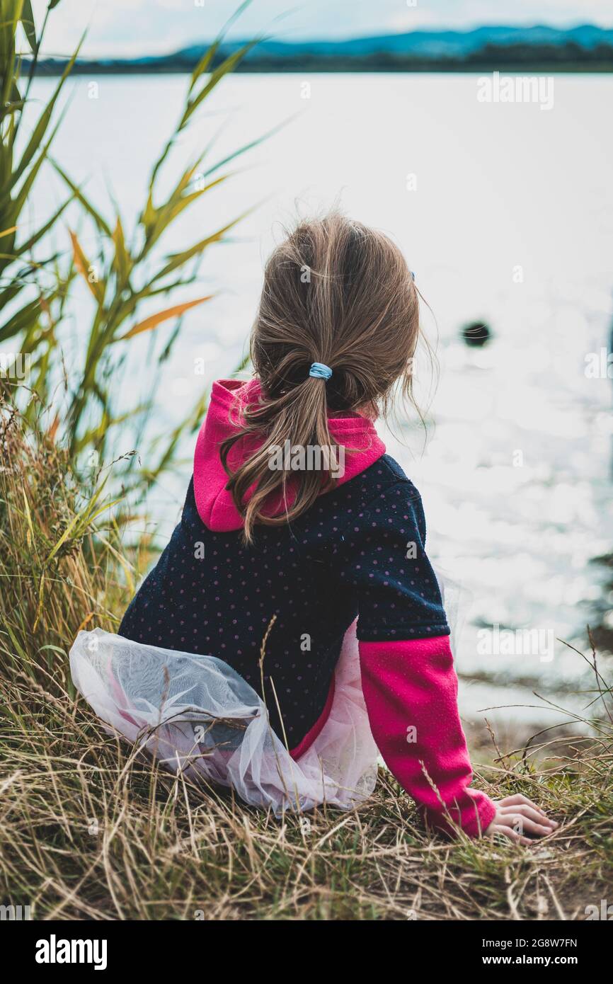 Kleines Mädchen, das am Ufer des Sees sitzt Stockfoto