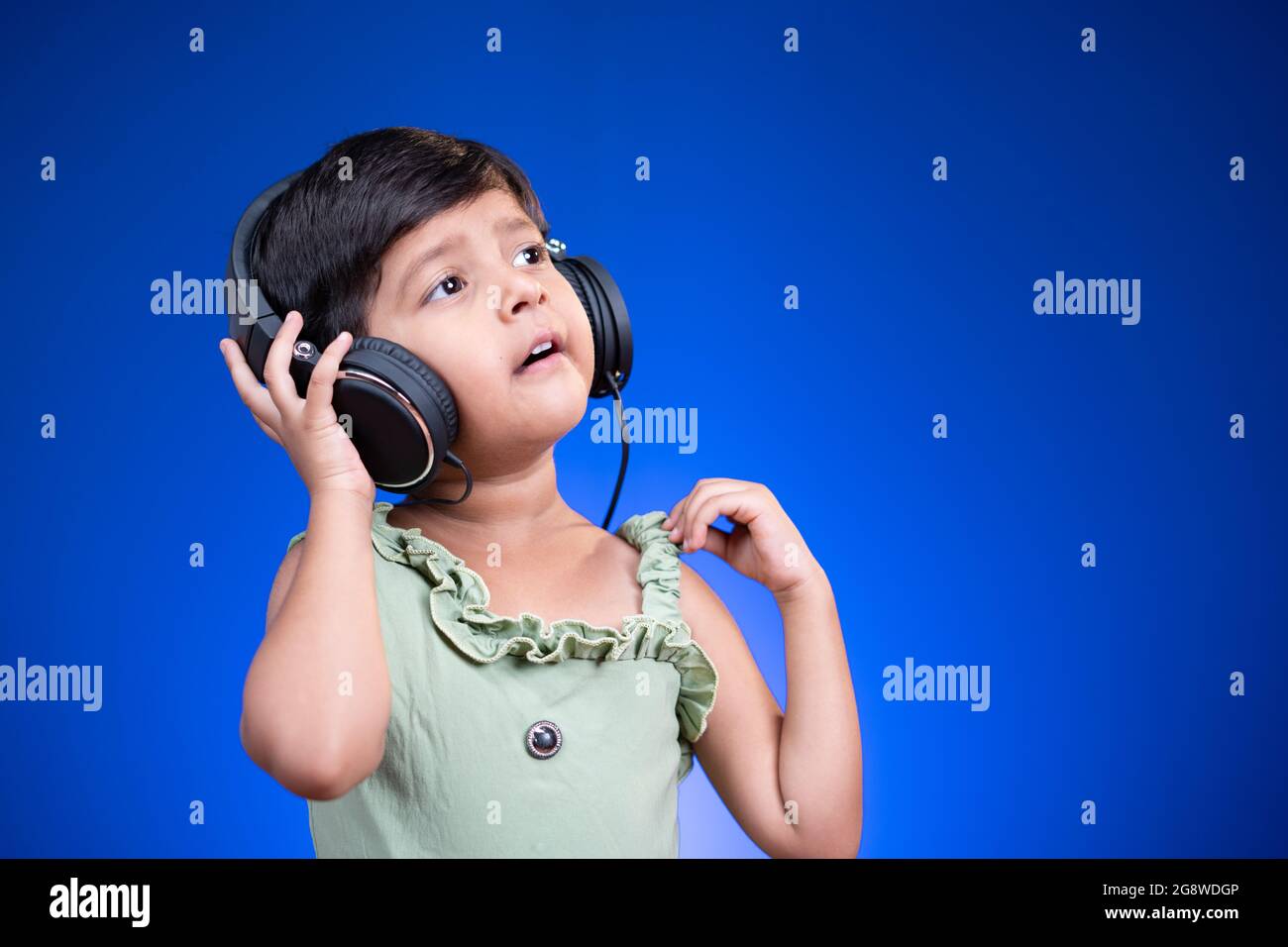 Fröhliches kleines Kind mit Kopfhörern, das auf blauem Hintergrund laut singt und dabei das Lieblingslied genießt. Stockfoto