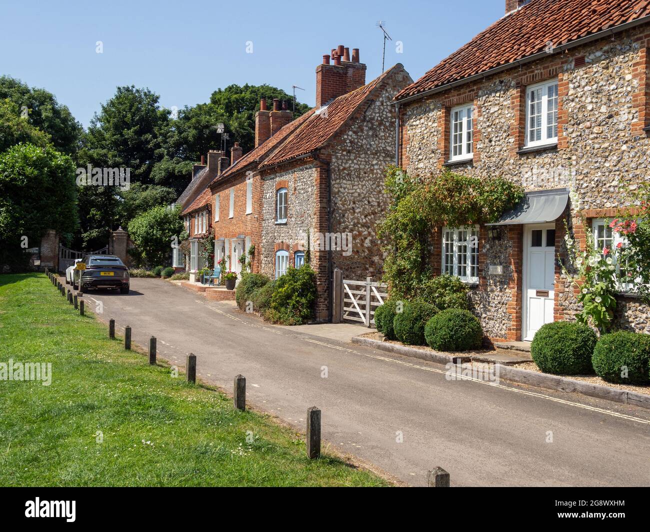 Straßenszene im Sommer im hübschen Dorf Burnham Market, Norfolk, Großbritannien; Reihe von Feuersteinhütten mit Blick auf das Grün. Stockfoto