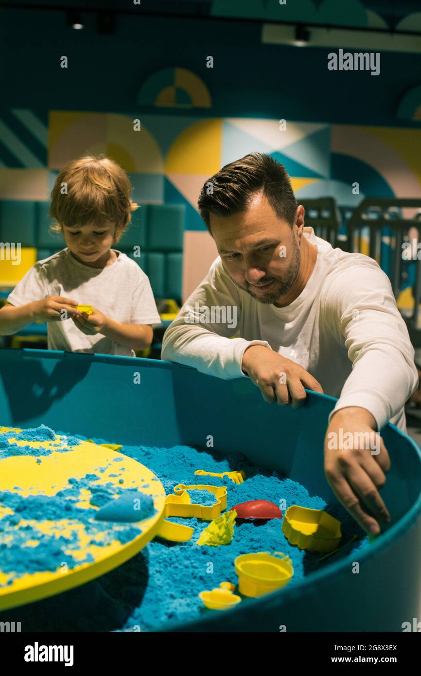 Boy und sein Vater c verwenden verschiedene Formen, um Figuren aus kinetischem Sand zu machen. Entwicklung von Feinmotorik. Kreativität und Selbstheilung. Auf Gegenseitigkeit Stockfoto