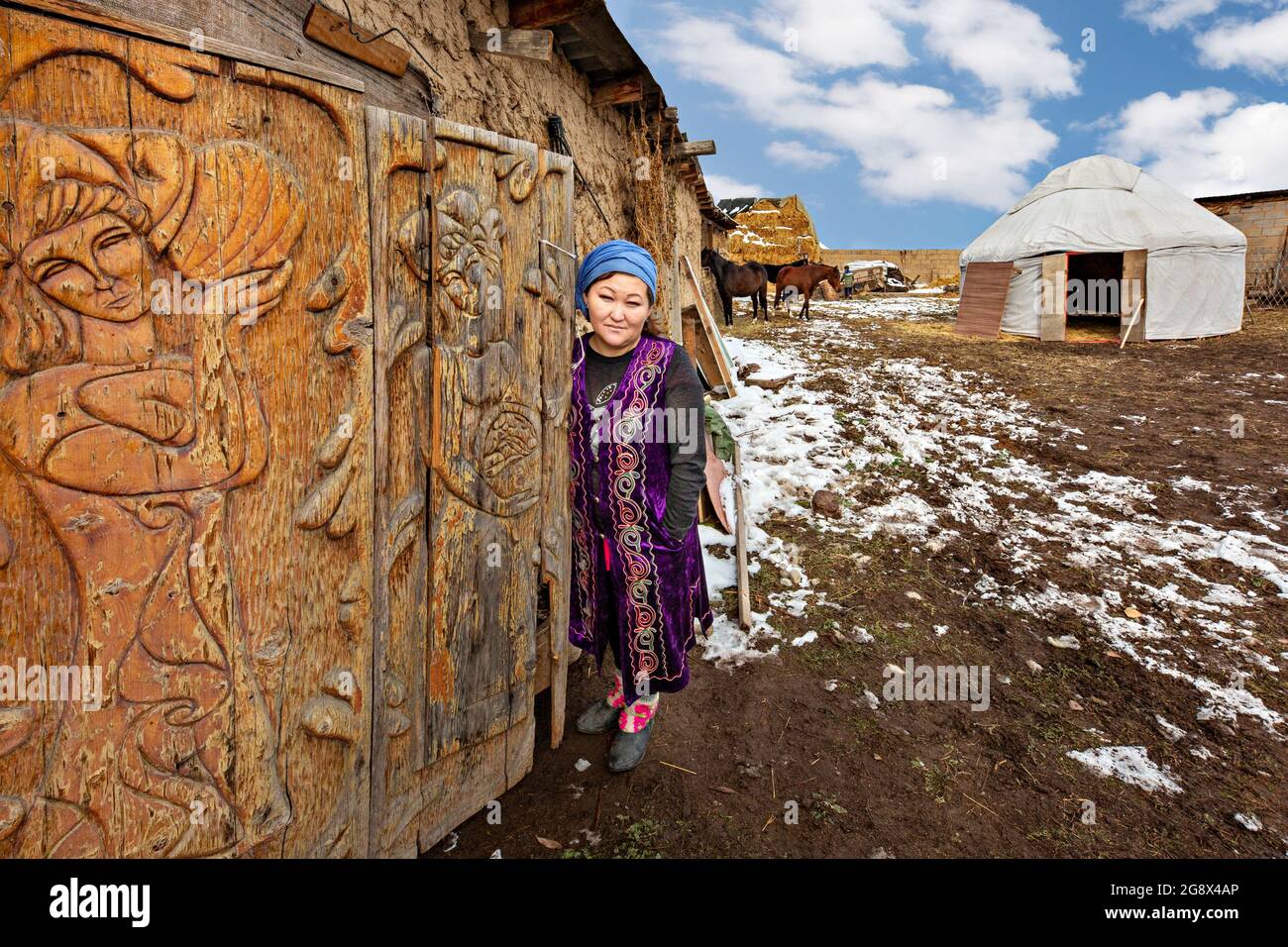 Kirgisin in traditioneller Kleidung mit geschnitzter Tür im Vordergrund und einer nomadischen Jurte im Hintergrund bei Bischkek, Kirgisistan Stockfoto