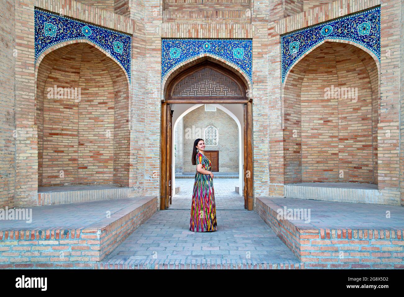 Usbekische Frau in einheimischer Kleidung mit dem Barak Khan Madrasa im Hintergrund Stockfoto