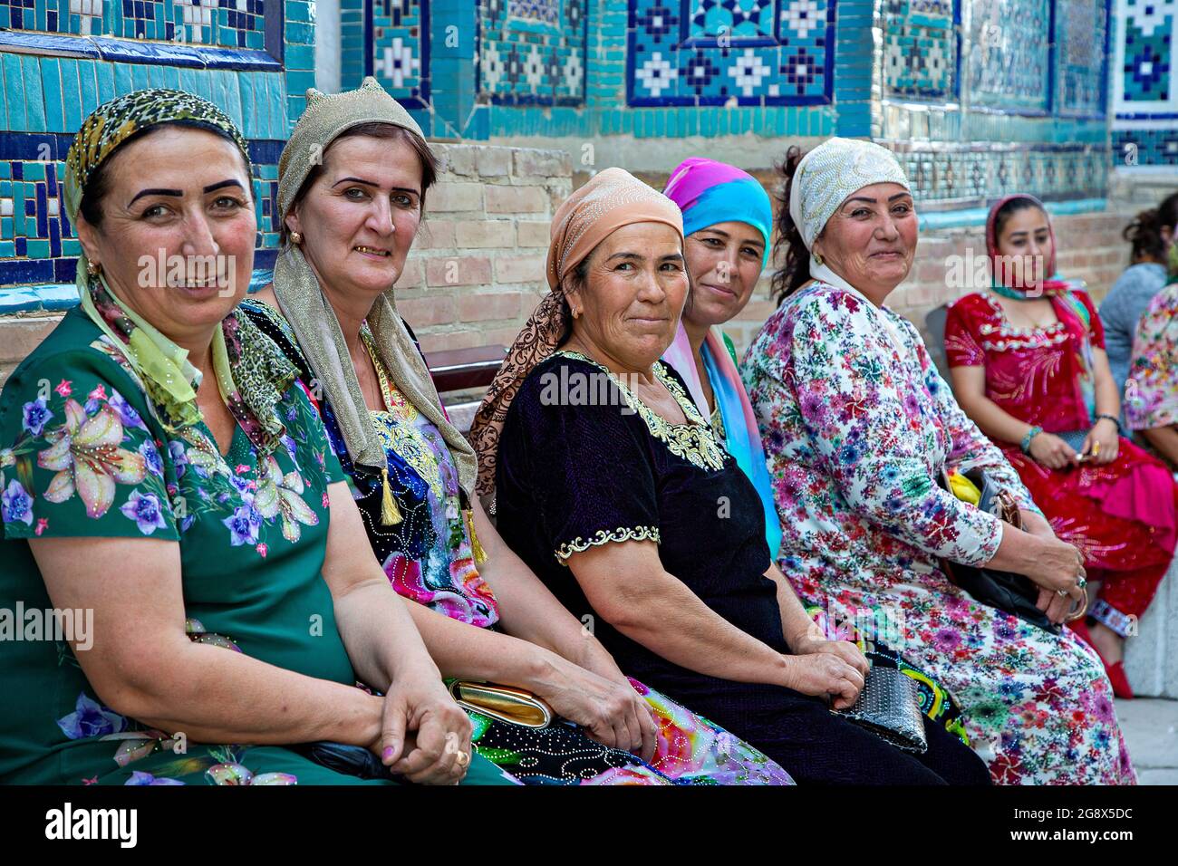 Frauen in bunten, traditionellen Kleidern sitzen und ruhen im Innenhof des Shahi Zinda Religious Complex in Samarkand, Usbekistan. Stockfoto