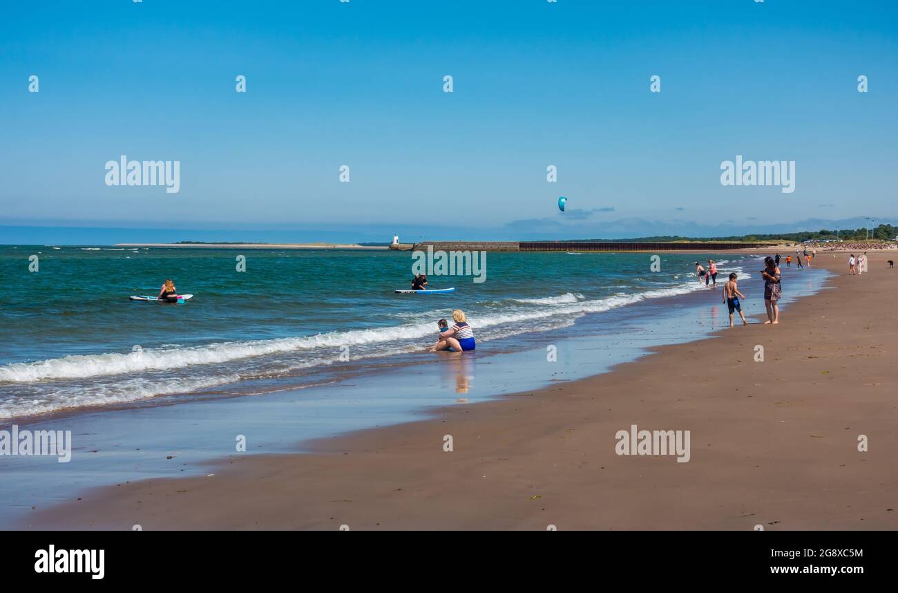 Sonnenanbeter und Schwimmer am Strand von Nairn, Schottland, an einem sonnigen Sommertag. Stockfoto