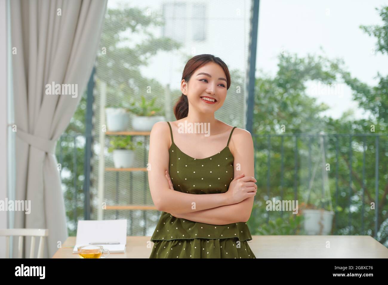 Junge schöne asiatische Frau trägt Polka Dots Kleid stehend aussehende Kamera mit gekreuzten Armen Stockfoto