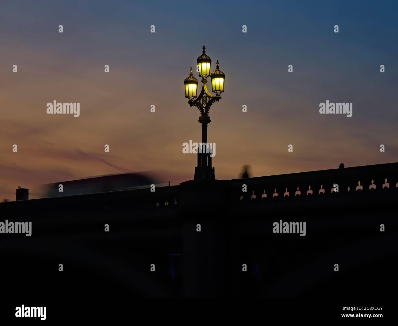 Eine schlichtschlüssige Aussicht auf die Brüstung der Westminster Bridge, wo eine gotische Straßenlaterne steht und ein London Bus und eine Person im Bild stehen. Stockfoto