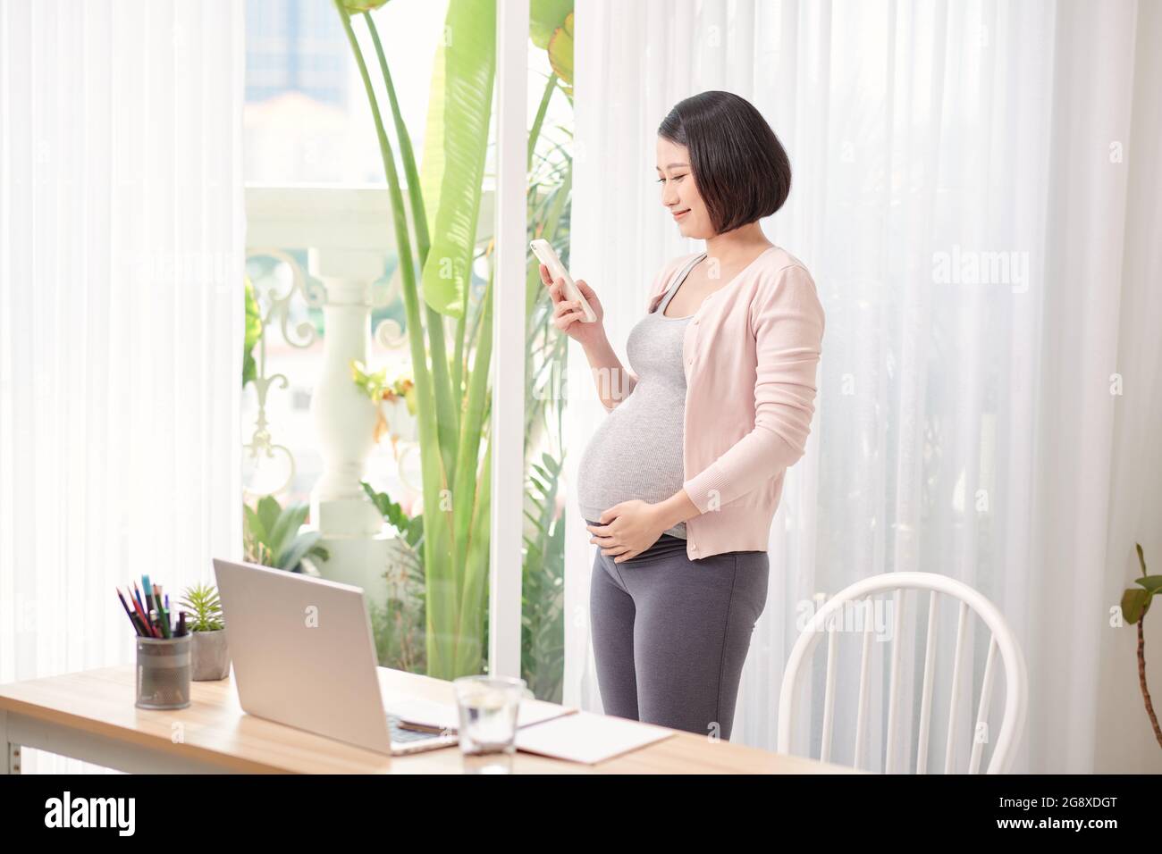 Schwanger asiatische Frau arbeitet von zu Hause in modernen Büro kontaktieren mit Handy im Gespräch, Stockfoto