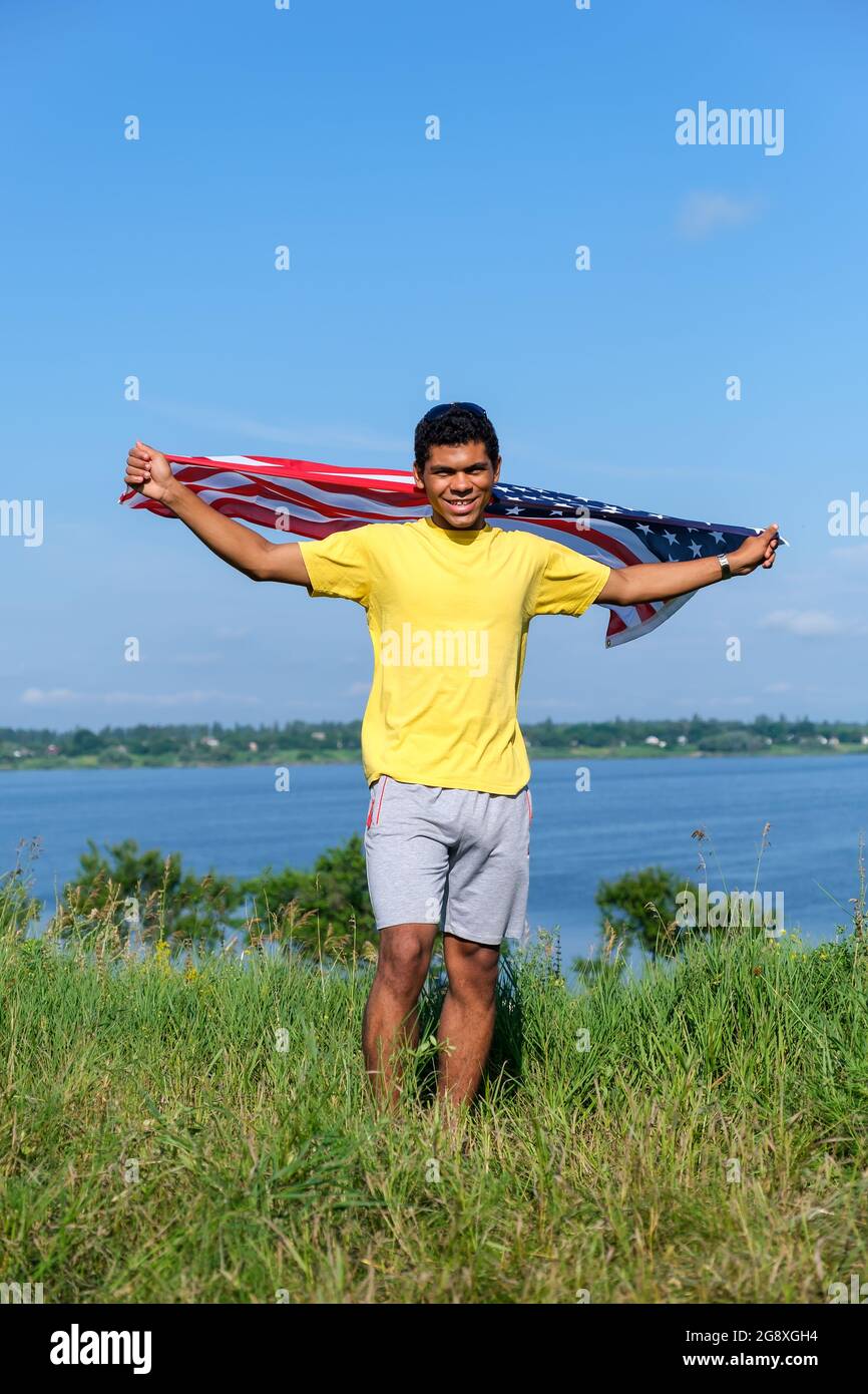 Junger afroamerikanischer Mann, der mit ausgestreckten Armen und US-Flagge steht Stockfoto