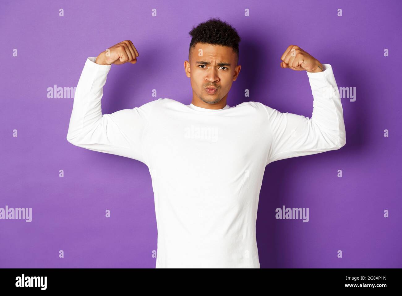 Bild von selbstbewussten afroamerikanischen jungen Kerl, Biegen Bizeps und versuchen zu zeigen, zeigt Muskeln nach dem Training, stehen über lila Hintergrund Stockfoto