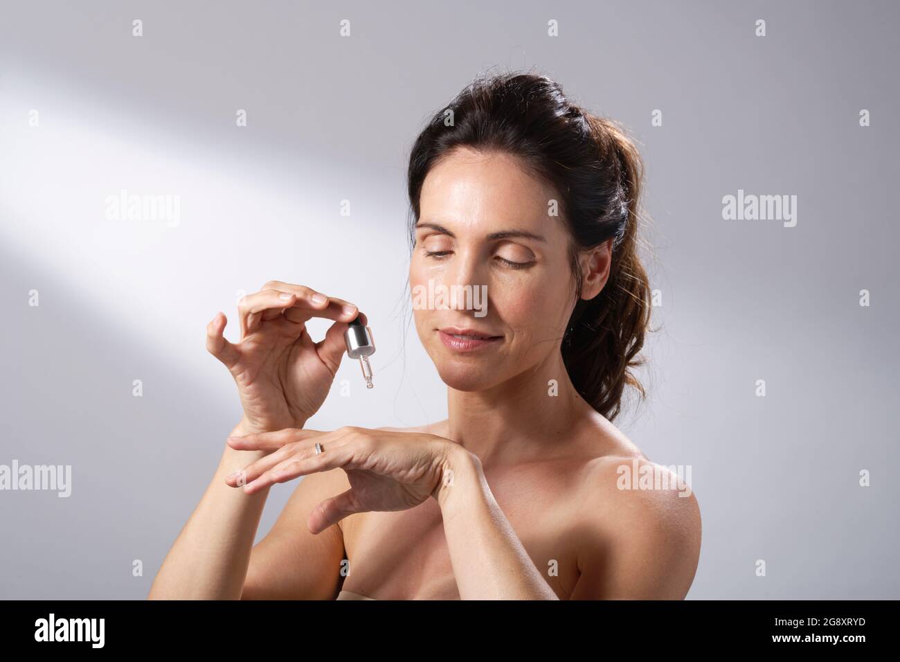 Eine junge Frau, die eine flüssige Pipette verwendet, um ihre Hände mit Hautpflege zu bespreizen. Stockfoto