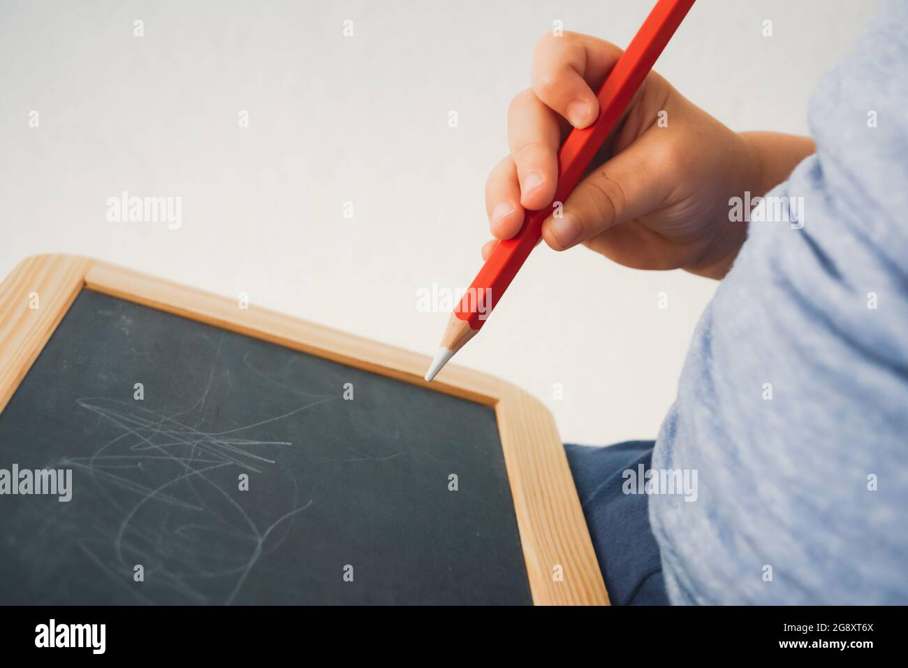 Kleinkind hält Kreidestift in der Hand und versucht, auf Tafel zu schreiben - kleiner Junge hält Kreide und schreibt, zeichnet auf Tafel Stockfoto