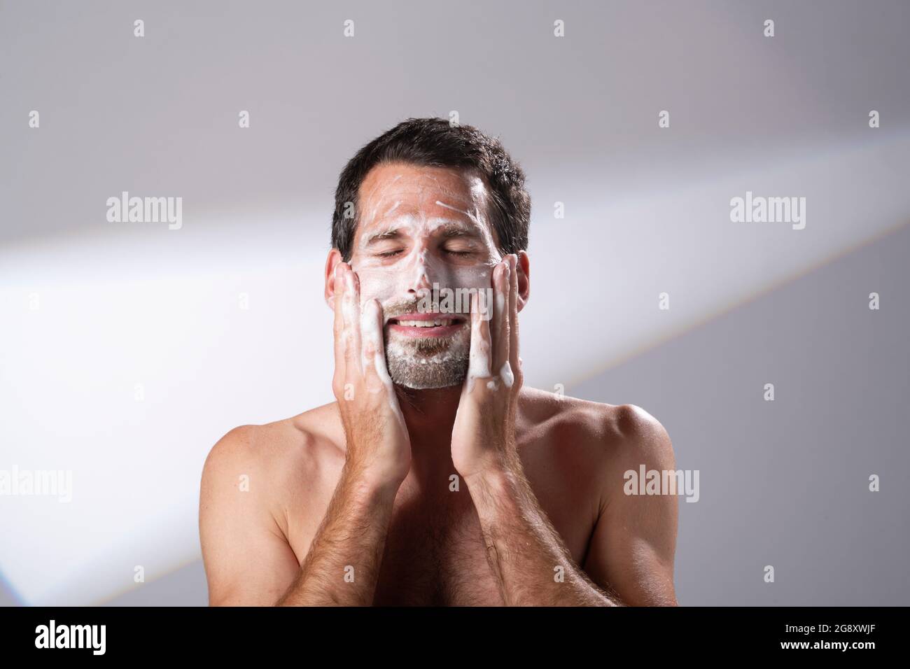 Mann, der eine Gesichtswäsche auf seine Haut aufgetragen hat. Seifenlauge wäscht sein Gesicht. Stockfoto