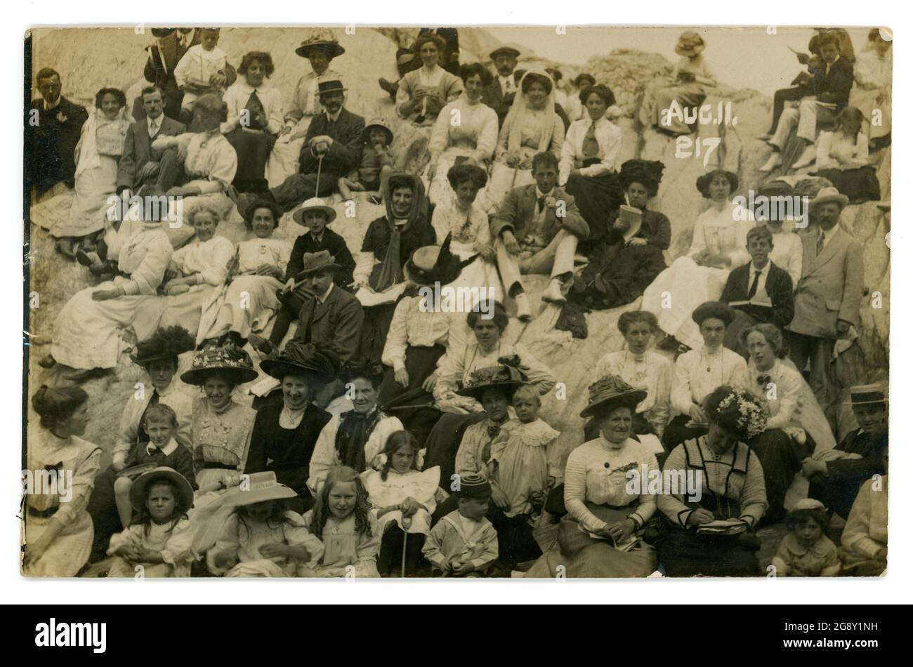 Edwardianische Postkarte von Strandgängern, die auf Felsen sitzen und ihre Sonntagsbestzeiten tragen, Foto der Strandfotografen Phillipse & Lees, Ilfracombe, Devon, Großbritannien vom 11 1910. August Stockfoto