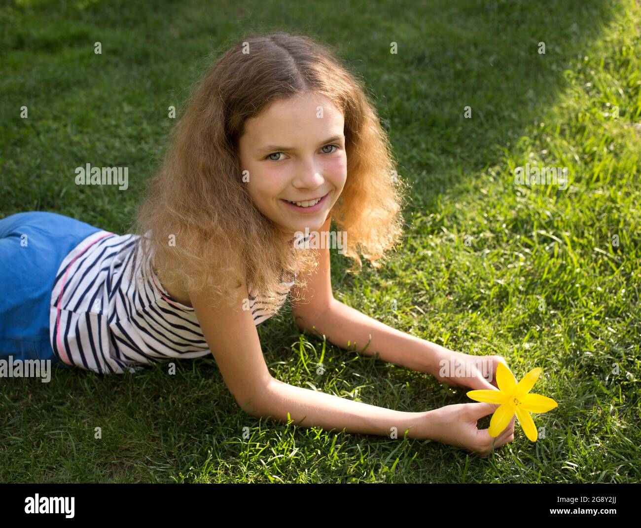 Porträt eines schönen lächelnden Teenager-Mädchen 12 Jahre alt auf dem Gras liegen an einem sonnigen Sommertag. Genuss von Ferien, Entspannung, Träume. Freudig Stockfoto