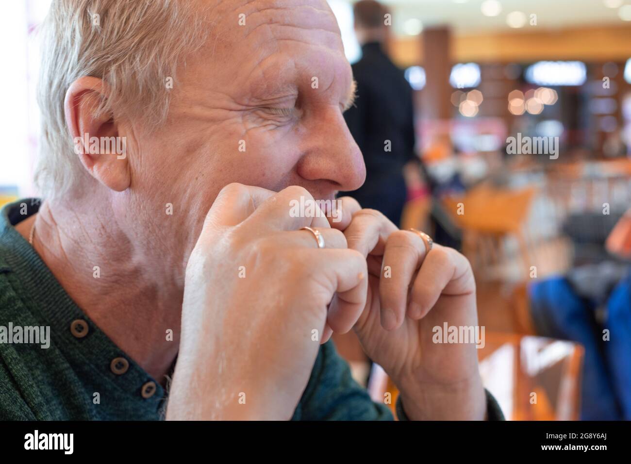 Reifer Mann, der mit den Händen in einem Café Essen isst und die Augen schließt Stockfoto