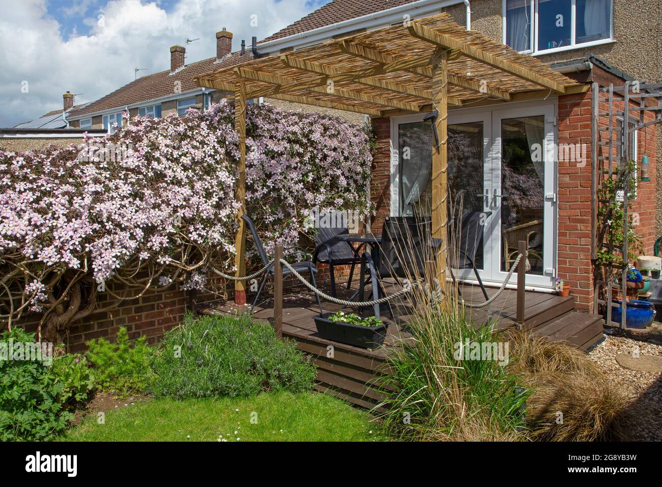 Englischer Garten mit Holzterrasse und Pergola und Clematis, die an einem Zaun wachsen Stockfoto