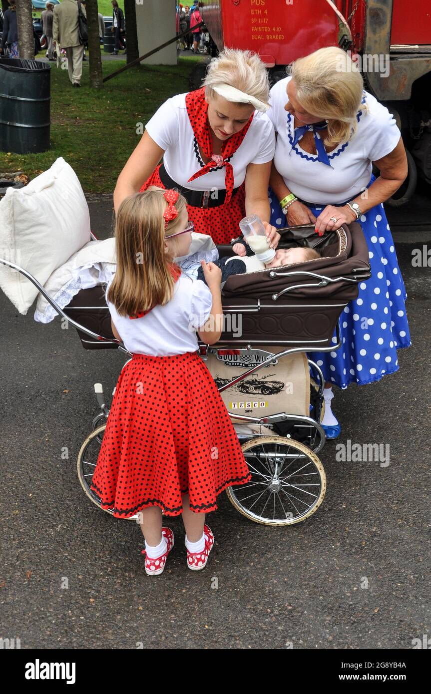 Frauen und Kinder im Stil der 1950er Jahre haben beim Goodwood Revival  Rockabilly-Röcke mit Punktmuster und weiße Oberteile. Baby in einem  altmodischen Kinderwagen. Retro-Event Stockfotografie - Alamy