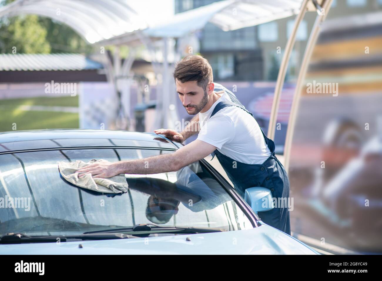 Mann in Arbeitskleidung, der ein Glas Auto abwischt Stockfoto