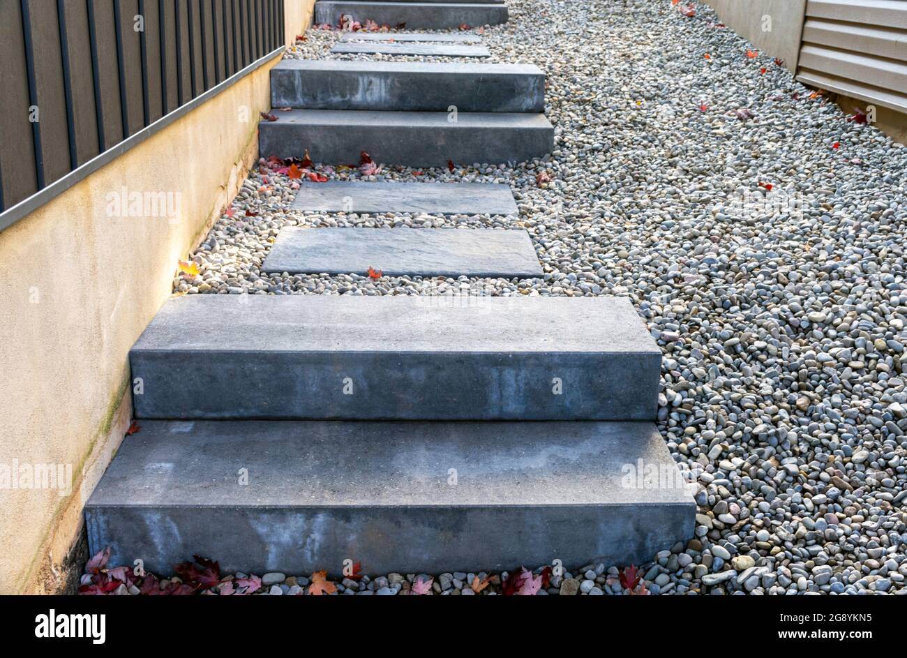 Betonfertigtreppen mit Trittsteinen und Flussfelsen entlang der Seite eines Hauses bieten einen sicheren Übergang vom Seitenhof zum Hinterhof unten. Stockfoto