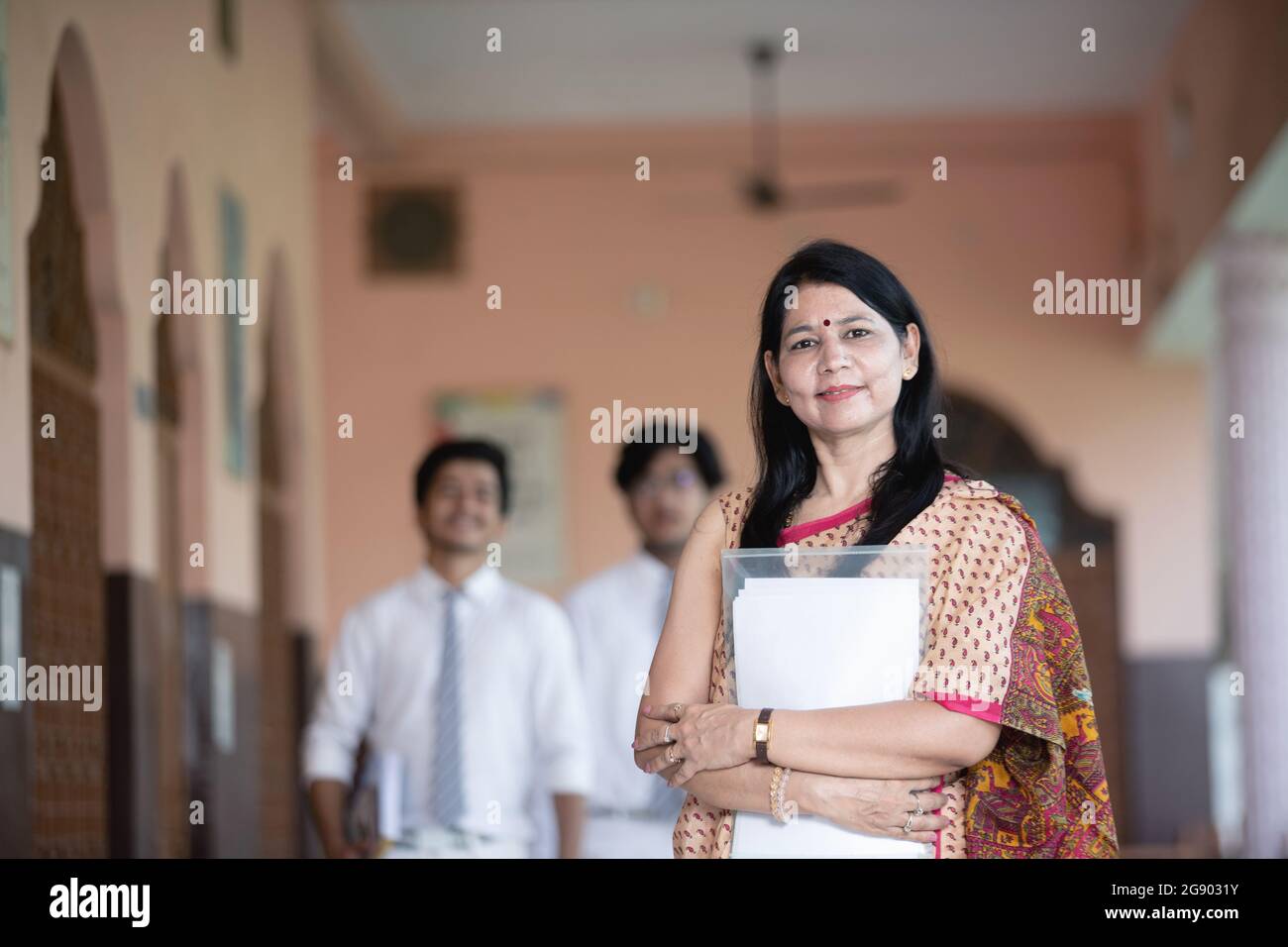 Low-Angle-Aufnahme eines selbstbewussten lächelnden indischen Lehrers mit Schülern im Hintergrund Stockfoto