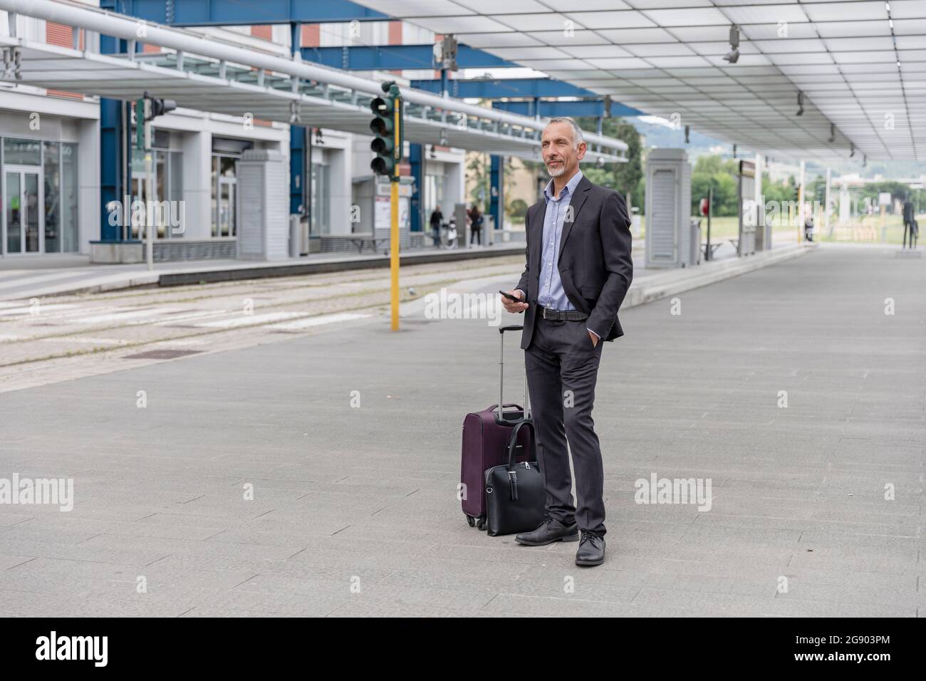 Geschäftsmann mit Gepäck wartet am Bahnhof auf den Zug Stockfoto