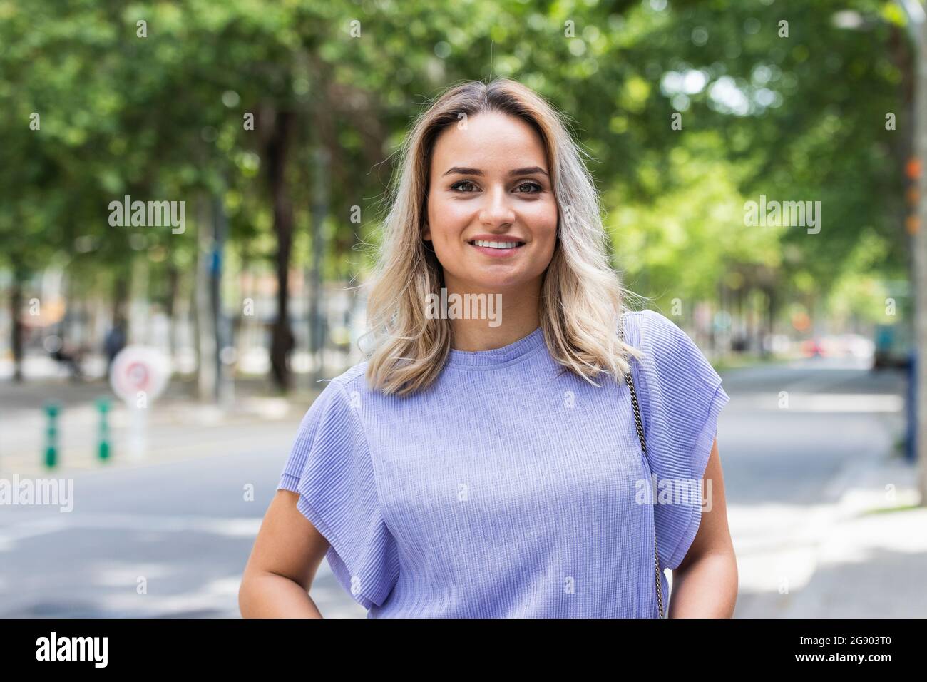 Lächelnde junge Frau mit blonden Haaren, die auf der Straße stehen Stockfoto