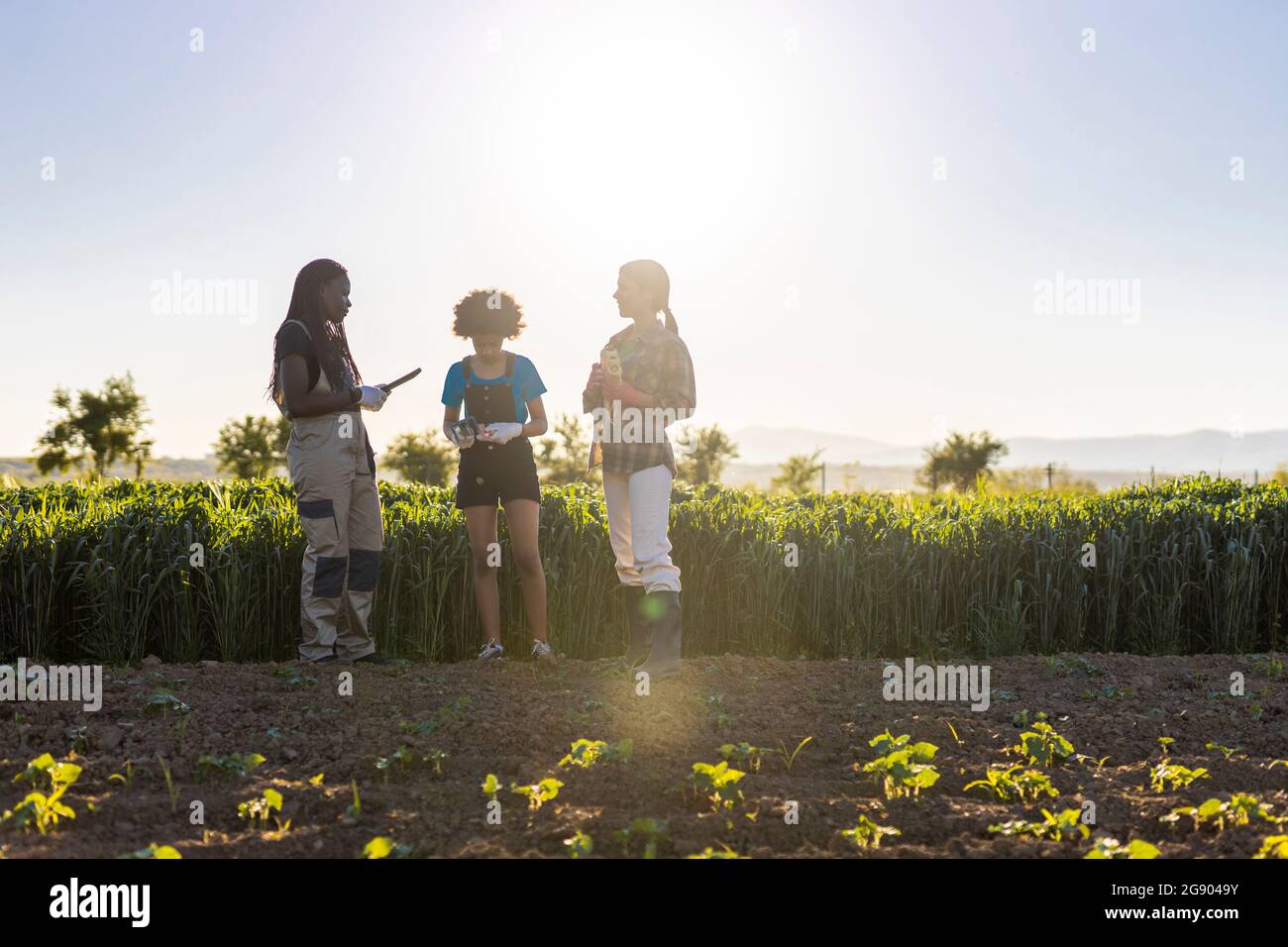 Farmerinnen, die an sonnigen Tagen mit Mädchen auf dem Bauernhof diskutieren Stockfoto