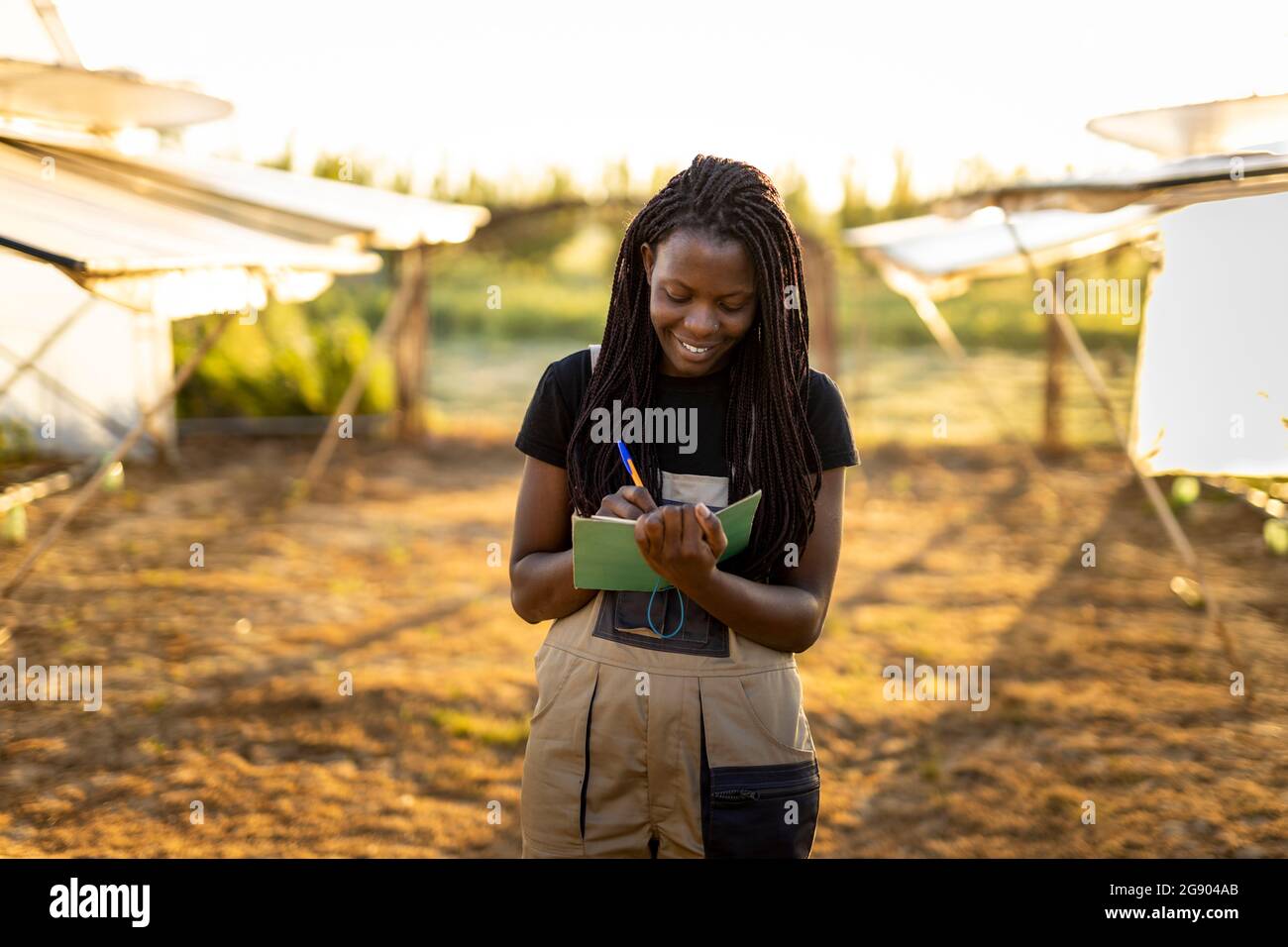 Lächelnde Bäuerin mit langen Haaren auf Notizblock, während sie auf der Farm steht Stockfoto