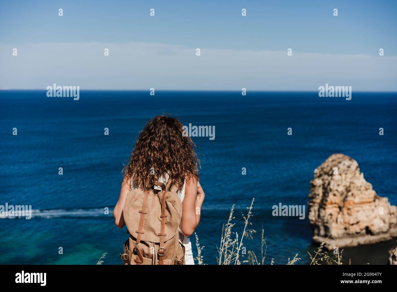 Backpacker-Frau, die an einem sonnigen Tag aufs Meer blickt Stockfoto