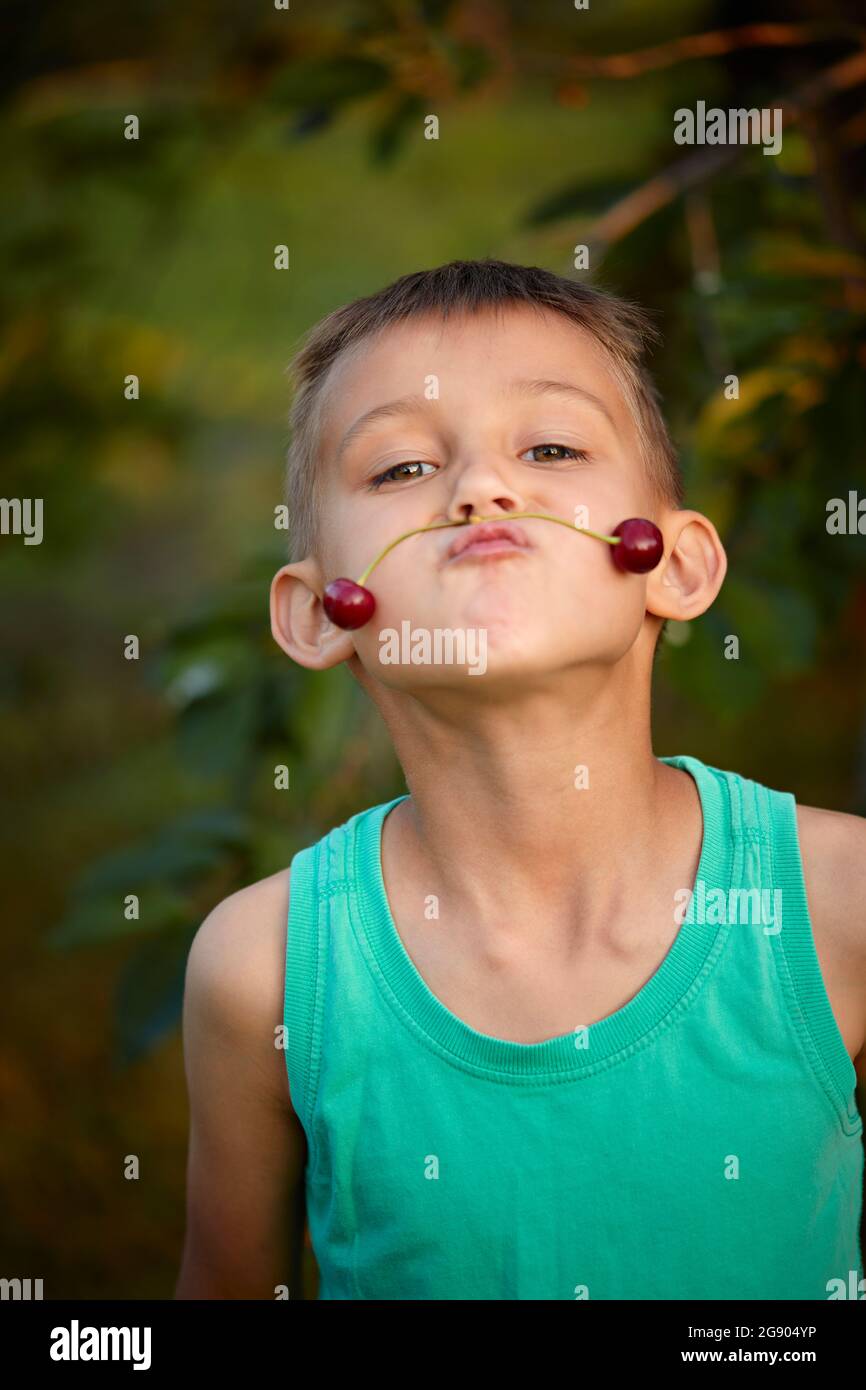 Junge puckert beim Balancieren von Kirschen auf dem Mund als Schnurrbart Stockfoto