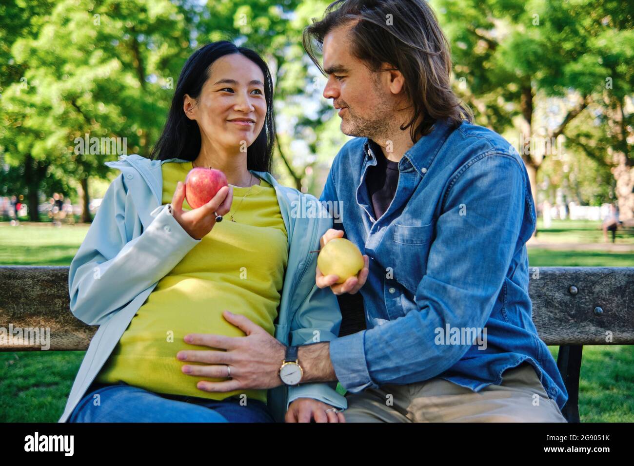 Fürsorglicher Ehemann mit der Hand auf dem Bauch der Frau, während er im öffentlichen Park saß Stockfoto