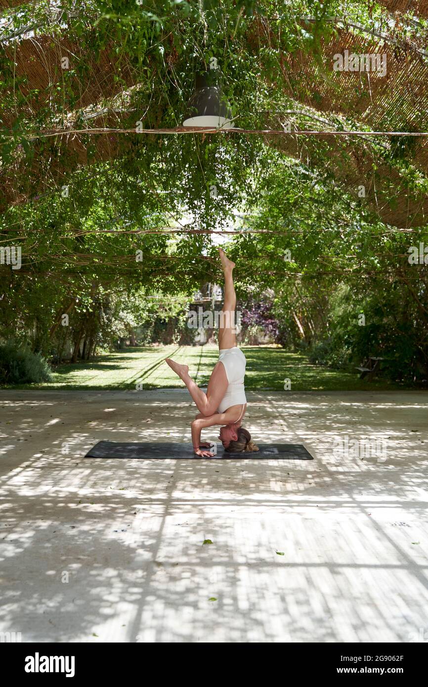 Reife Frau übt Kopfstand auf Yoga-Matte im Garten Stockfoto